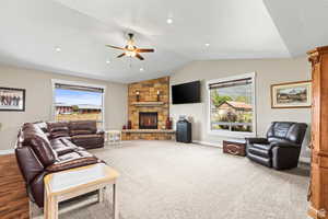 Living area with a ceiling fan, a stone fireplace, and light carpet