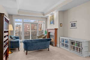 Living area featuring a raised ceiling, crown molding, a glass covered fireplace, and carpet floors