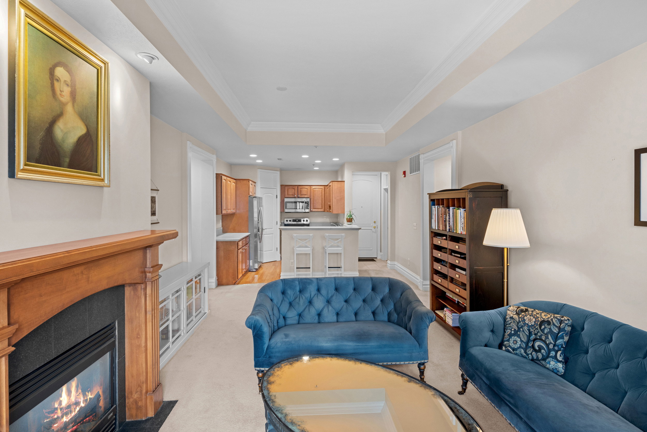 Living area featuring crown molding, a raised ceiling, recessed lighting, light carpet, and a fireplace with flush hearth