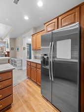 Kitchen with stainless steel refrigerator with ice dispenser, light countertops, light wood finished floors, recessed lighting, and wood finish cabinetry
