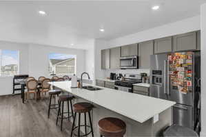 Kitchen with gray cabinets, stainless steel appliances, a kitchen breakfast bar, wood finished floors, and an island with sink