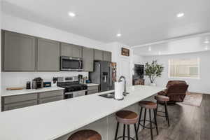 Kitchen featuring gray cabinets, stainless steel appliances, a kitchen breakfast bar, and recessed lighting