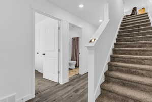 Staircase with wood finished floors and recessed lighting