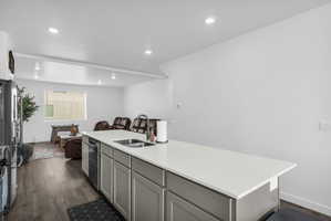 Kitchen with open floor plan, a center island with sink, dark wood-type flooring, stainless steel appliances, and gray cabinetry