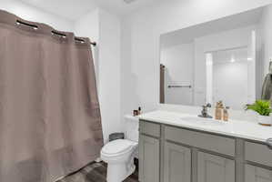 Full bath featuring curtained shower, vanity, and dark wood-style floors