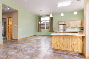 Kitchen with light wood finish cabinets, concrete floors, stainless steel appliances, suspended lighting, and light countertops