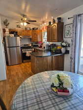 Kitchen with dark countertops, stainless steel appliances, a peninsula, wood finish cabinets, and a ceiling fan