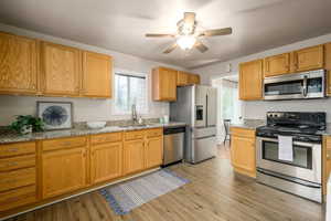Kitchen with stainless steel appliances, ceiling fan, light stone countertops, and light wood-type flooring
