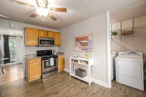 Kitchen featuring stainless steel appliances, a ceiling fan, separate washer and dryer, light wood-type flooring, and light stone countertops