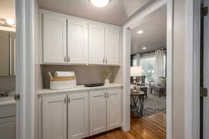 Bar area featuring dark wood-style flooring, white cabinetry, recessed lighting, and light stone counters