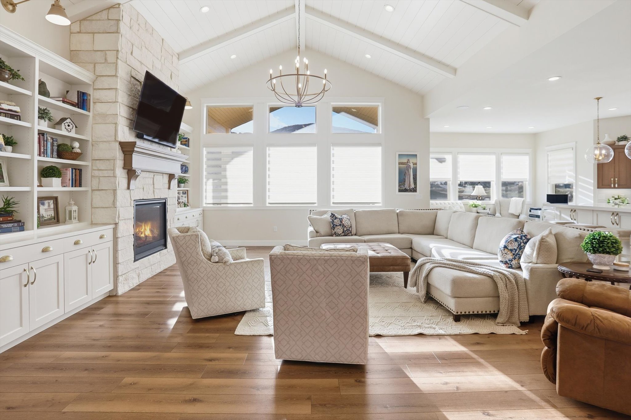 Living room with a chandelier, light wood finished floors, and a stone fireplace