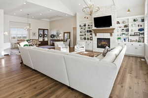 Living area with suspended lighting, lofted ceiling, hardwood / wood-style flooring, and a stone fireplace