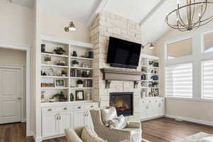 Living area with dark wood-style flooring, a stone fireplace, suspended lighting, lofted ceiling with beams, and wooden ceiling