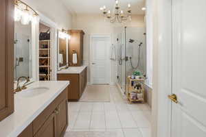 Full bathroom featuring a chandelier, a stall shower, two vanities, and light tile patterned floors