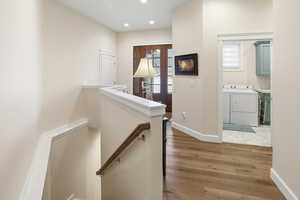 Hall featuring light wood-style flooring, an upstairs landing, washing machine and dryer, and recessed lighting