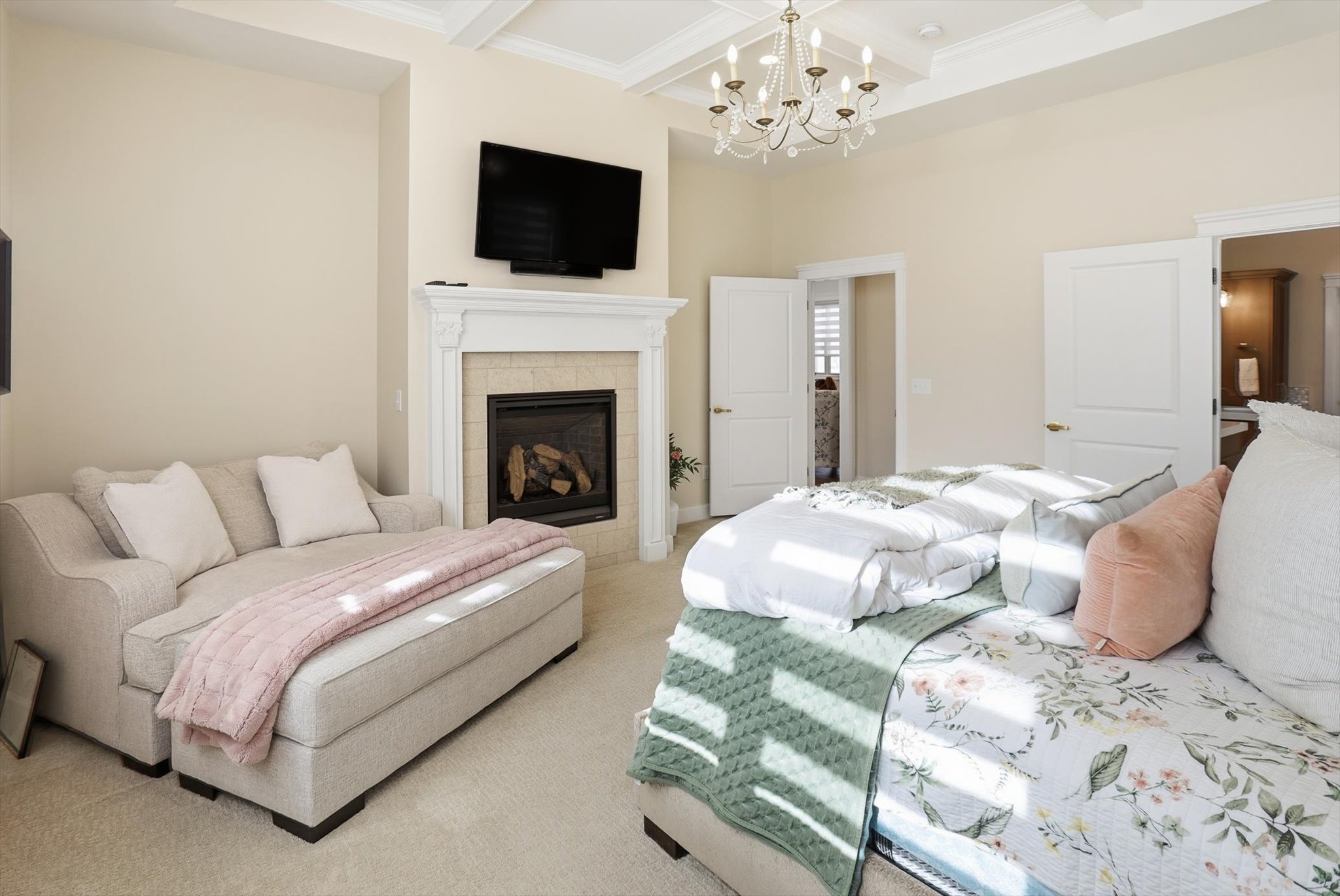 Carpeted bedroom with coffered ceiling, a chandelier, a tile fireplace, and crown molding