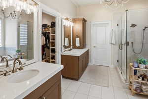 Bathroom featuring suspended lighting, two vanities, a shower stall, and a spacious closet