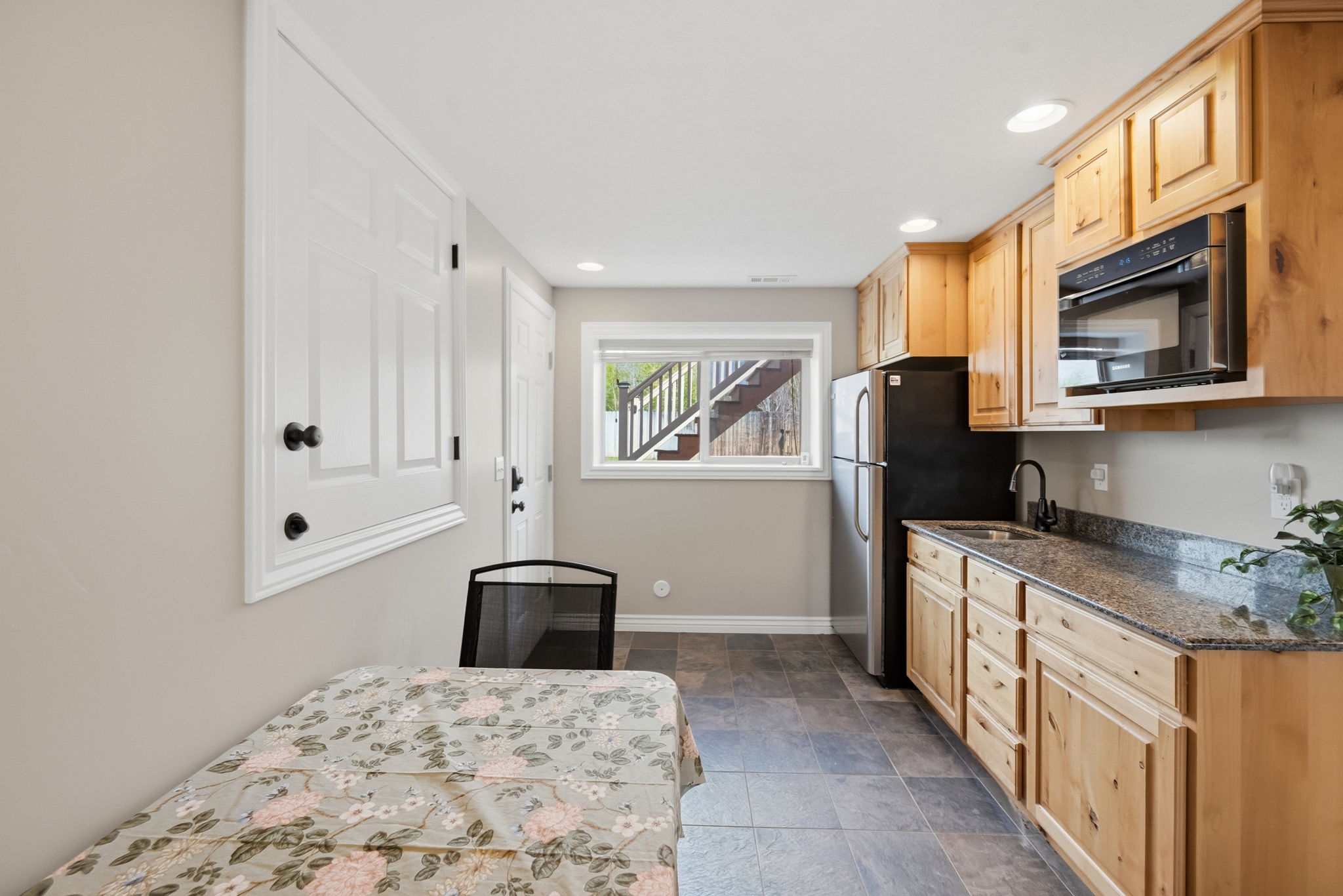 Kitchen featuring light wood finish cabinetry, freestanding refrigerator, dark stone finish floors, recessed lighting, and dark countertops