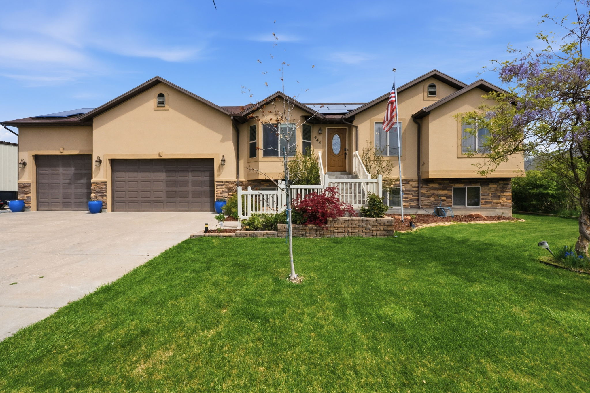 View of front of home featuring stone siding, a 3 car attached garage, solar panels, and driveway