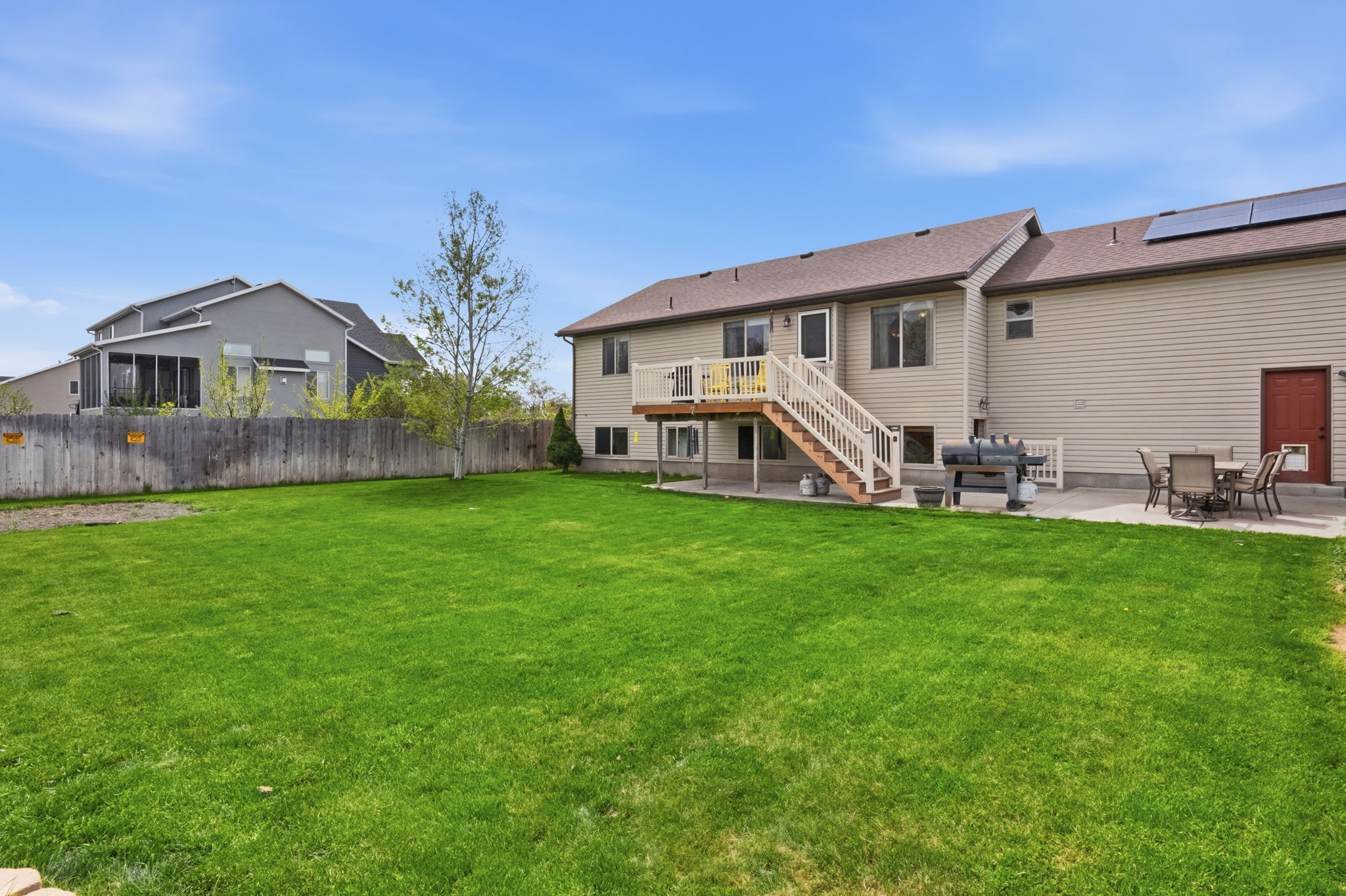 Back of house with a patio, roof mounted solar panels, a wooden deck, and outdoor dining space