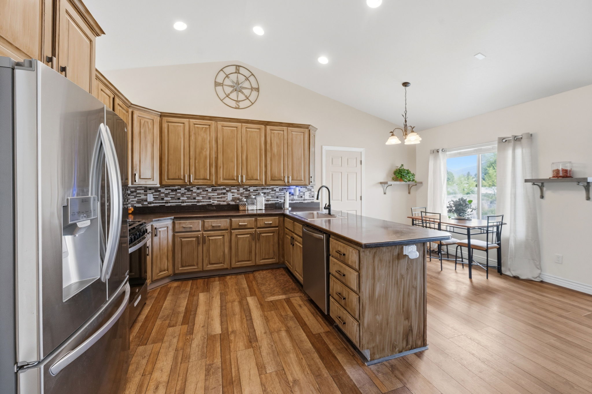Kitchen featuring stainless steel appliances, a peninsula, dark countertops, suspended lighting, and wood finish cabinetry