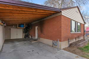 View of home's exterior featuring a carport, brick siding, a patio, and driveway