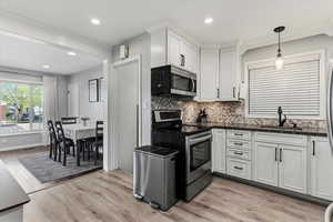 Kitchen featuring stainless steel appliances, backsplash, white cabinetry, light wood-type flooring, and decorative light fixtures