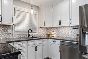 Kitchen featuring stainless steel appliances, white cabinetry, dark stone counters, decorative light fixtures, and backsplash