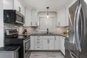 Kitchen with stainless steel appliances, white cabinetry, pendant lighting, and backsplash