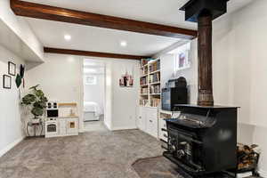 Home office featuring a wood stove, dark colored carpet, a textured ceiling, beam ceiling, and recessed lighting