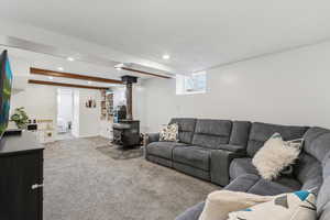 Living room with carpet floors, a wood stove, recessed lighting, a textured ceiling, and beam ceiling