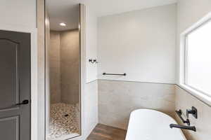 Full bathroom featuring tile walls, a soaking tub, a stall shower, wainscoting, and dark wood-type flooring
