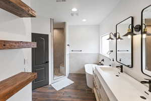 Full bath featuring double vanity, a walk in shower, a soaking tub, tile walls, and dark wood-style floors
