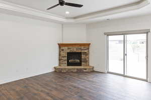 Unfurnished living room featuring a tray ceiling, dark wood finished floors, ceiling fan, a stone fireplace, and recessed lighting