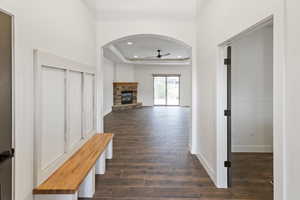 Corridor featuring a tray ceiling, dark wood-style flooring, recessed lighting, and arched walkways