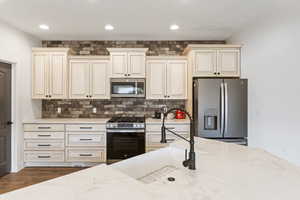 Kitchen with cream cabinets, stainless steel appliances, backsplash, light stone counters, and recessed lighting