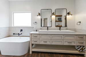 Full bathroom with double vanity, dark wood-style flooring, a freestanding tub, tile walls, and wainscoting