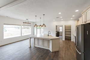 Kitchen with freestanding refrigerator, pendant lighting, cream cabinets, dark wood finished floors, and a kitchen breakfast bar