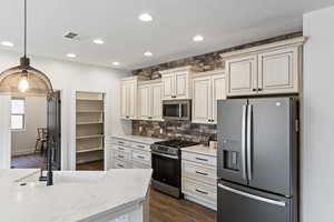 Kitchen with stainless steel appliances, light stone countertops, decorative light fixtures, and cream cabinets