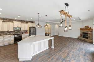Kitchen featuring cream cabinets, stainless steel appliances, arched walkways, a center island with sink, and open floor plan