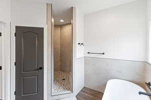 Full bath featuring tile walls, a soaking tub, a tile shower, dark wood finished floors, and wainscoting