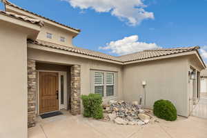 Doorway to property with stucco siding, stone siding, and a tile roof
