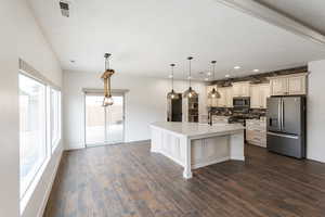 Kitchen with cream cabinetry, stainless steel appliances, decorative backsplash, hanging light fixtures, and dark wood-style flooring