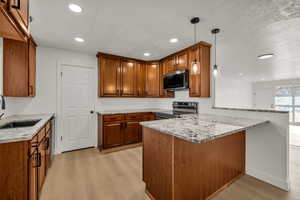 Kitchen with a peninsula, decorative light fixtures, wood finish cabinetry, light wood finished floors, and light stone counters