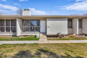 View of front of property featuring a front lawn, stucco siding, a chimney, and entry steps