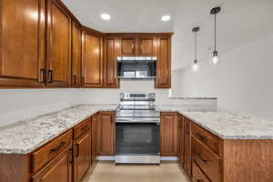 Kitchen with stainless steel appliances, wood finish cabinetry, a peninsula, and light stone countertops