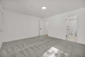 Unfurnished bedroom with light colored carpet and connected bathroom
