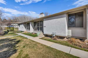 View of property exterior with a yard, stucco siding, a chimney, and entry steps