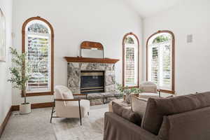 Carpeted living room with a stone fireplace and vaulted ceiling