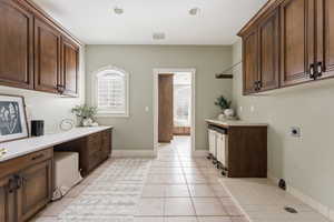 Laundry room featuring cabinet space, electric dryer hookup, light tile patterned flooring, and a desk